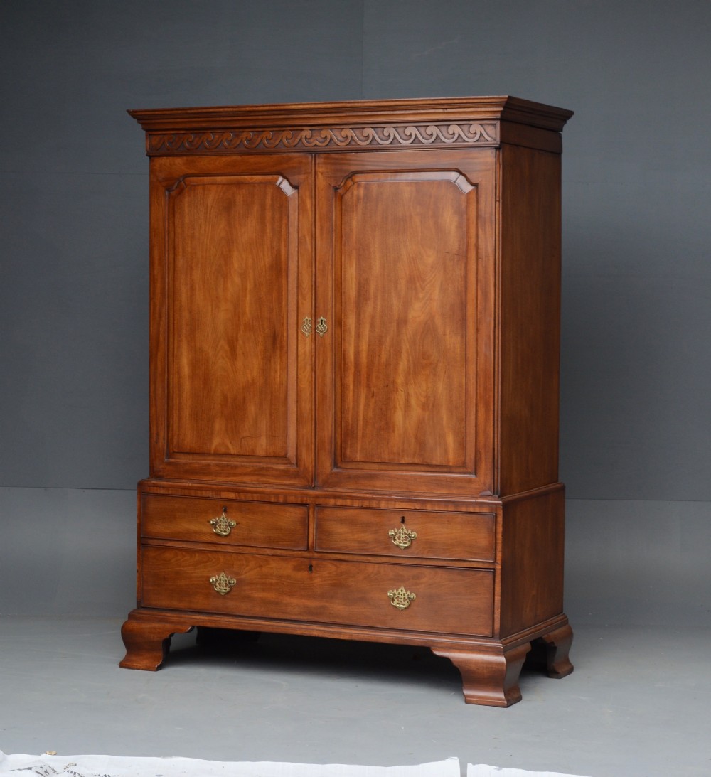 A Georgian mahogany gentlemans wardrobe featuring a carved frieze, double panelled doors, two short over one long drawer, and bracket feet. View III