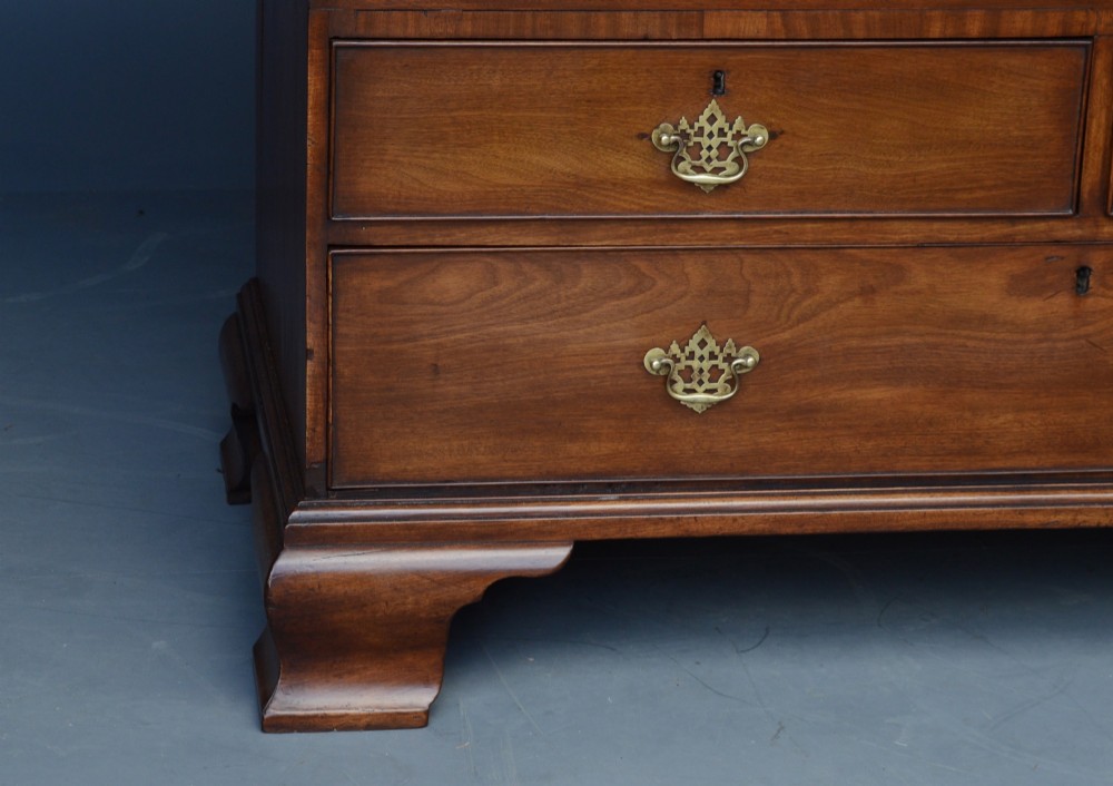 A Georgian mahogany gentlemans wardrobe featuring a carved frieze, double panelled doors, two short over one long drawer, and bracket feet. View VI