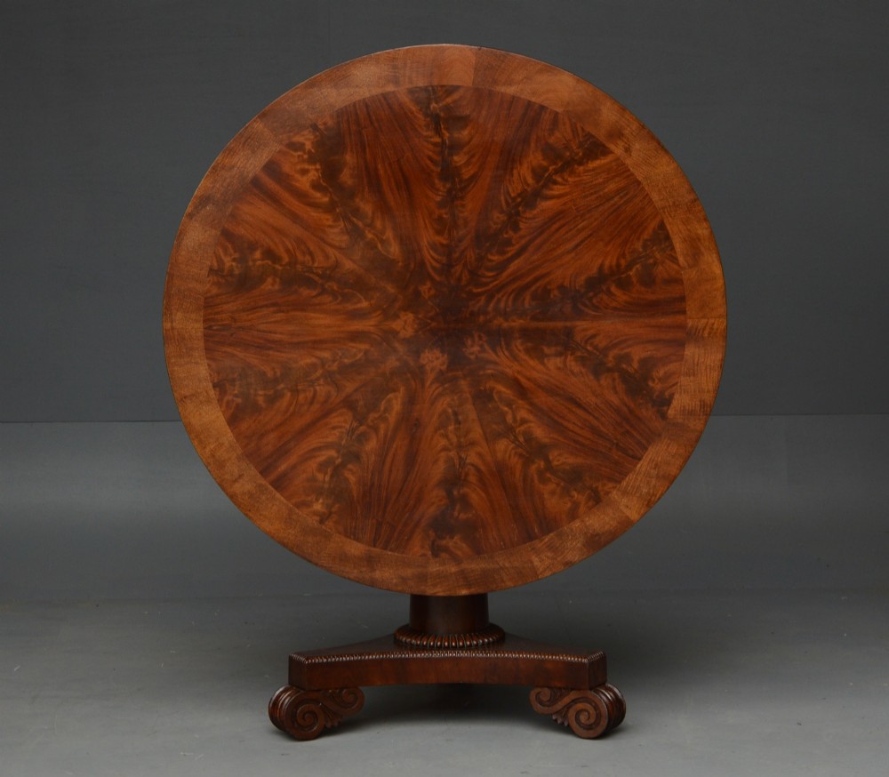 An early 19th-century Regency tilt-top table with a circular flame mahogany veneered top on a central pedestal base.