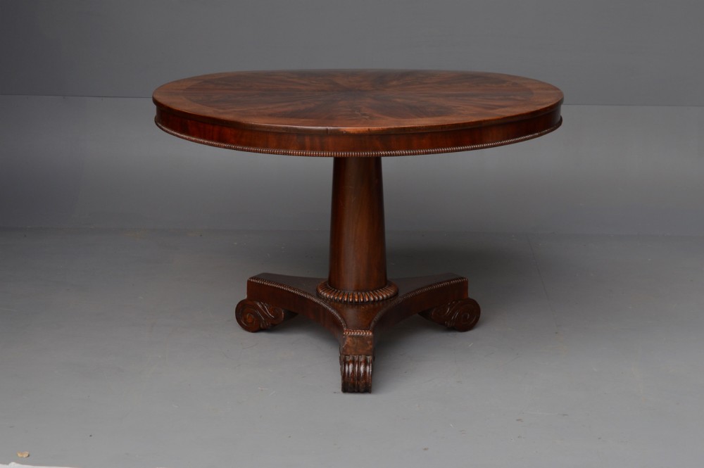 An early 19th-century Regency tilt-top table with a circular flame mahogany veneered top on a central pedestal base. View II