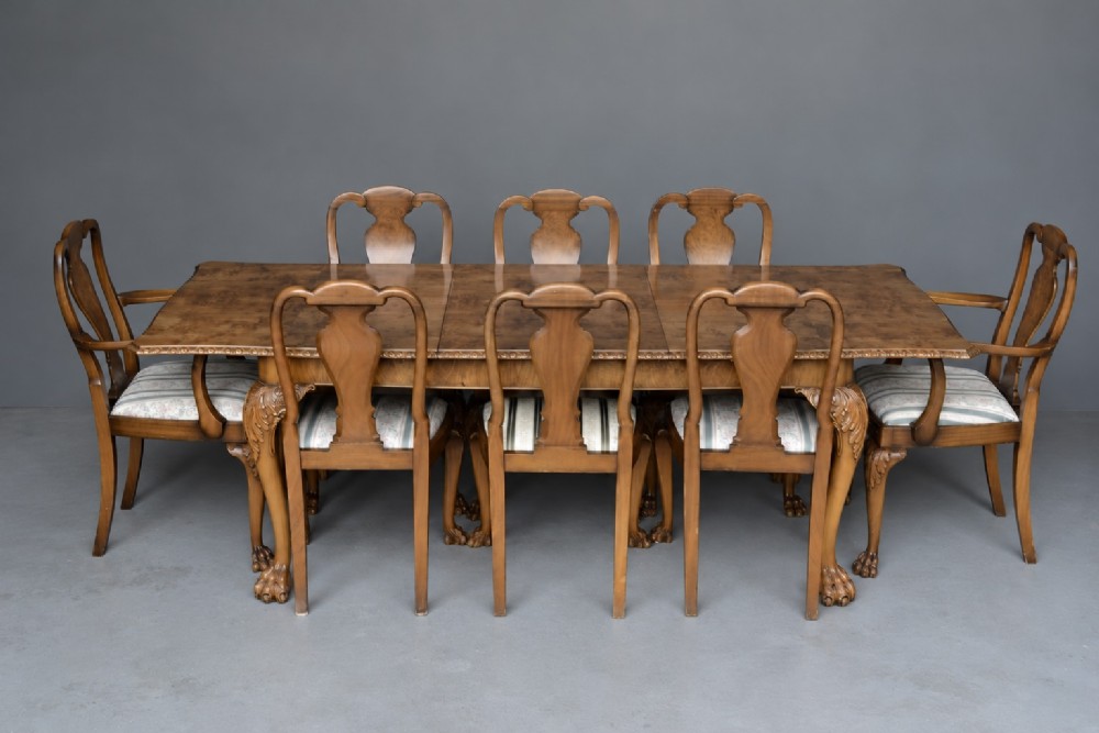 A figured walnut Queen Anne style extending dining table surrounded by eight matching splat-back chairs with carved cabriole legs and upholstered seat cushions.