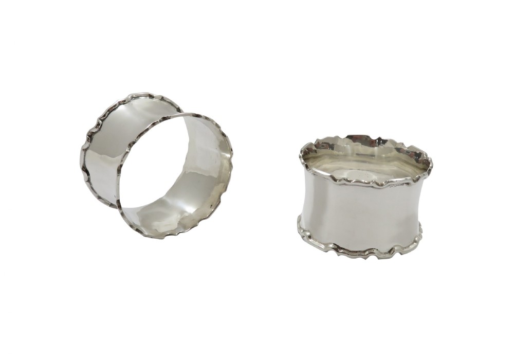 A pair of scalloped sterling silver napkin rings resting inside an open black fitted presentation case lined with cream silk. View II
