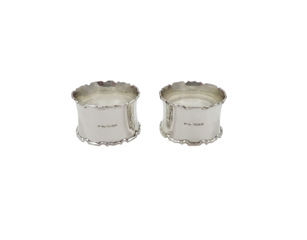 A pair of scalloped sterling silver napkin rings resting inside an open black fitted presentation case lined with cream silk. View V