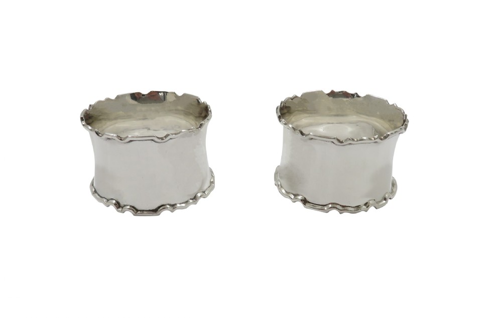 A pair of scalloped sterling silver napkin rings resting inside an open black fitted presentation case lined with cream silk. View VIII
