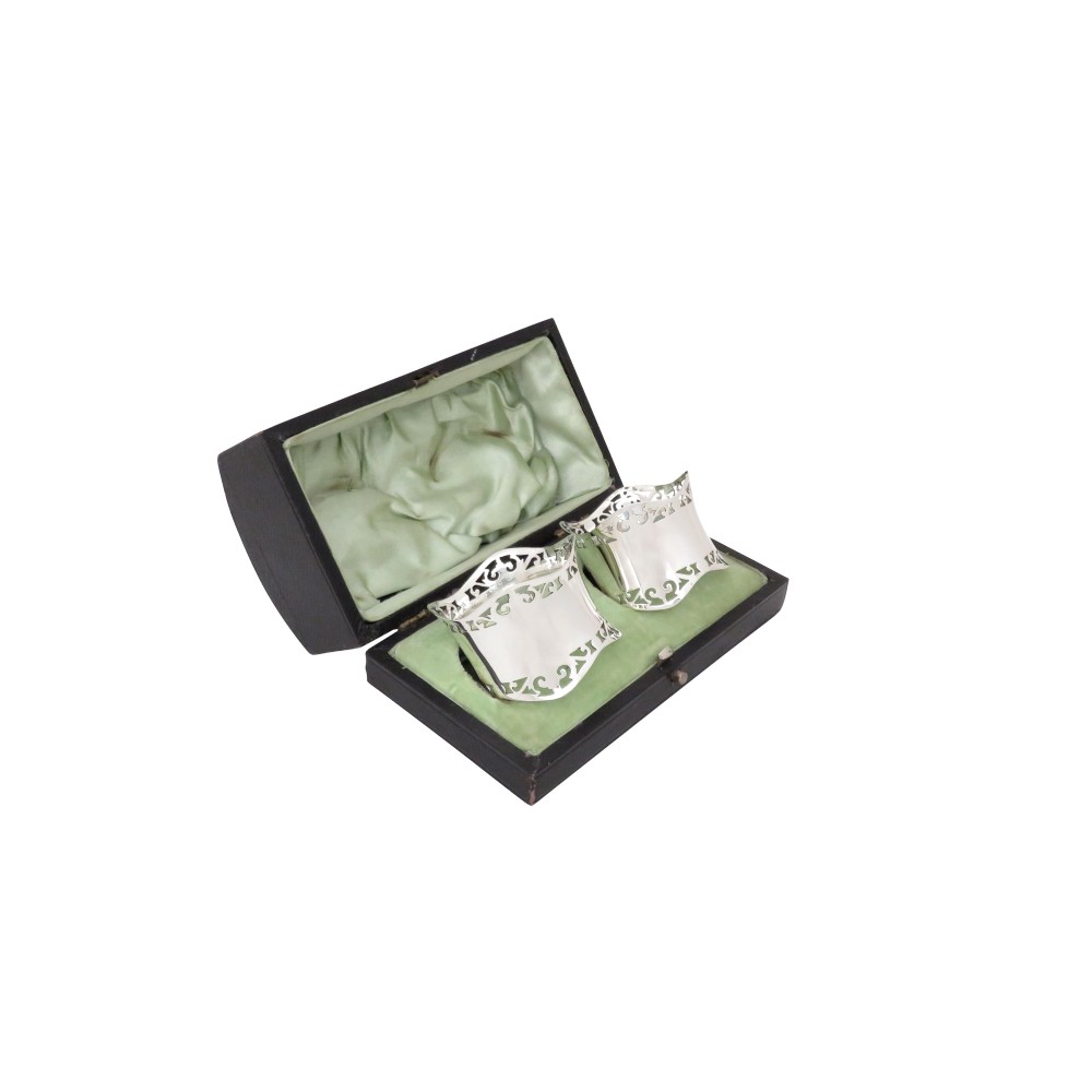 A pair of hallmarked sterling silver napkin rings with pierced borders, presented inside an open black fitted case lined with green satin.