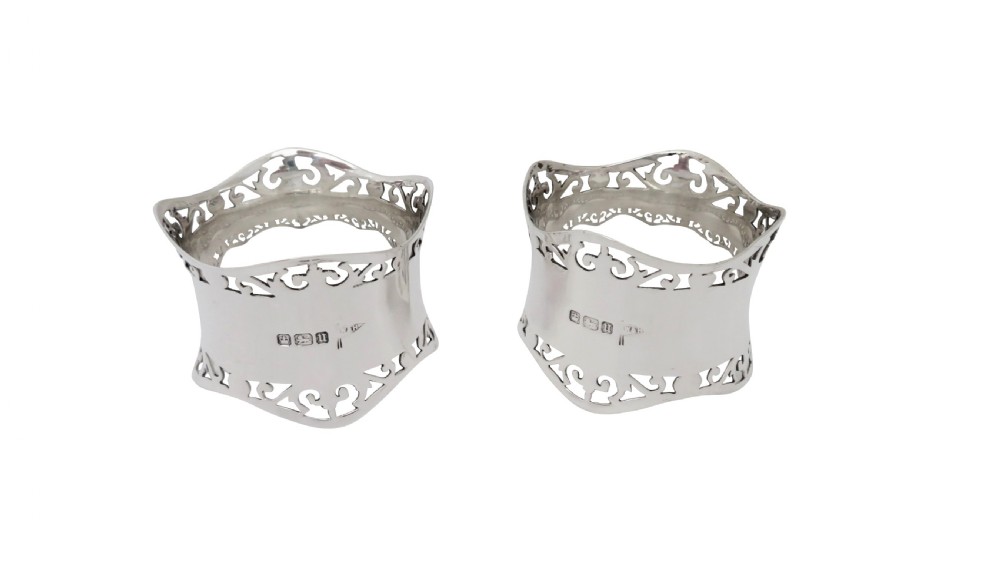 A pair of hallmarked sterling silver napkin rings with pierced borders, presented inside an open black fitted case lined with green satin. View II