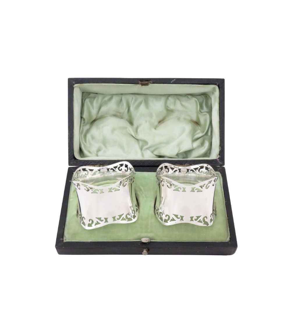 A pair of hallmarked sterling silver napkin rings with pierced borders, presented inside an open black fitted case lined with green satin. View IV