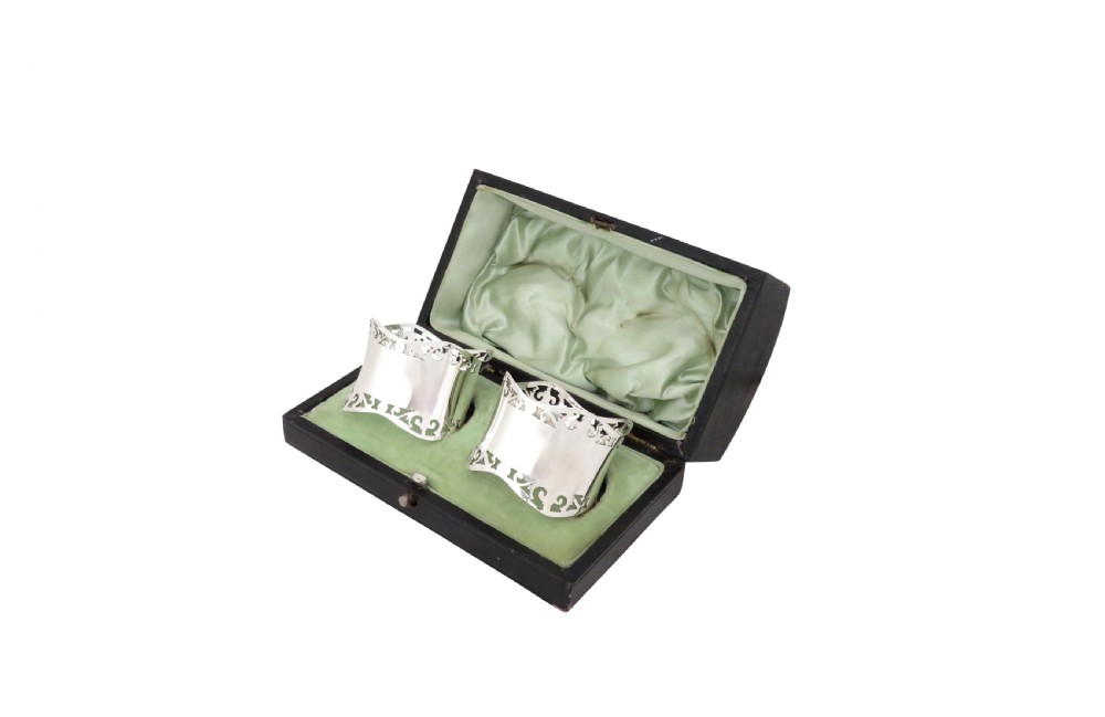 A pair of hallmarked sterling silver napkin rings with pierced borders, presented inside an open black fitted case lined with green satin. View VIII