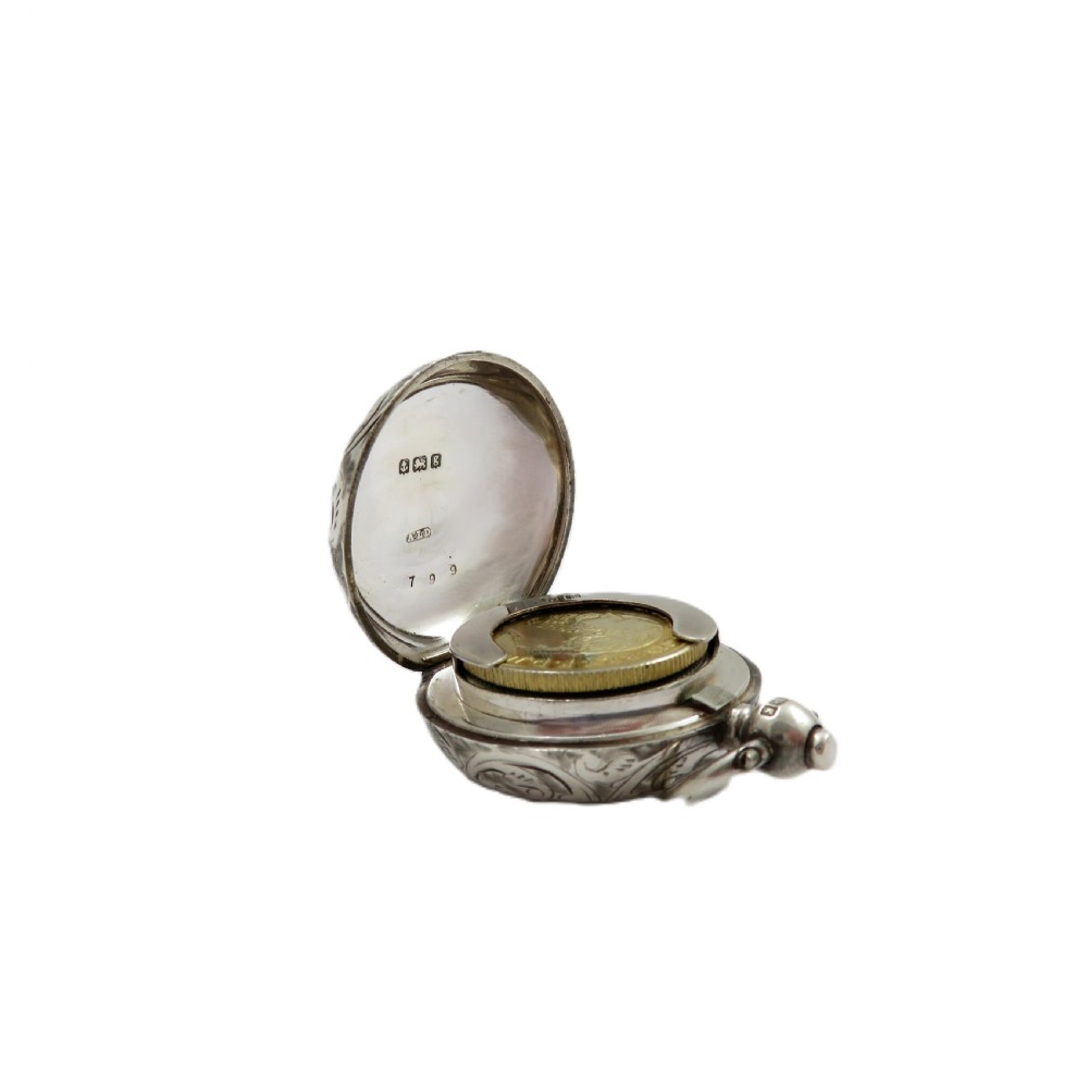 A circular Edwardian sterling silver sovereign case decorated with hand-engraved foliate scrollwork and featuring a top suspension ring. View VI