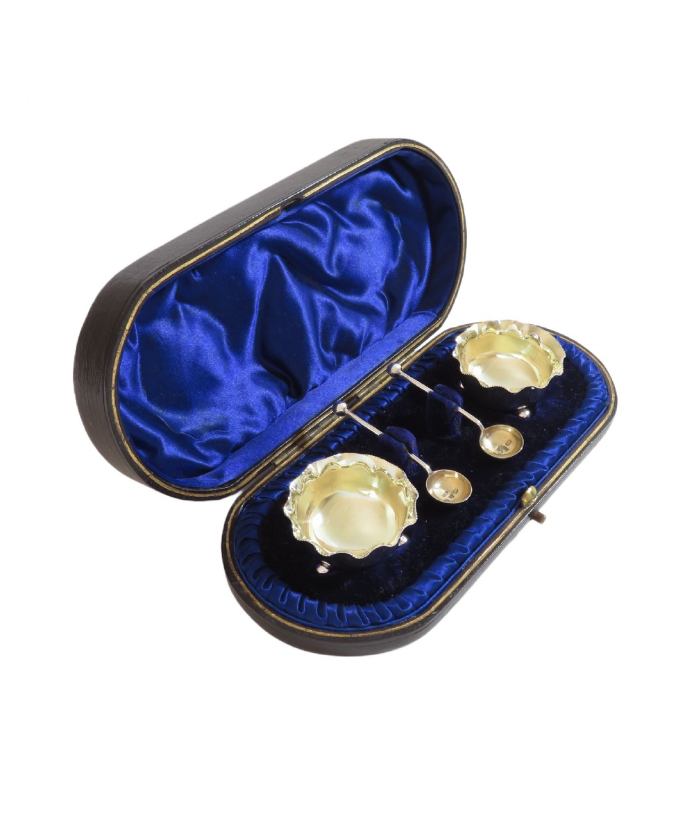 A pair of Victorian sterling silver open salt cellars with crimped rims and matching spoons set inside a blue velvet presentation case. View IX