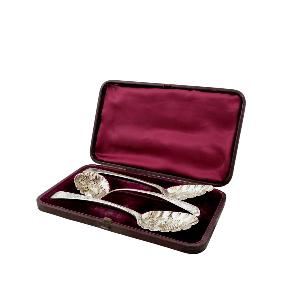 A fitted plum fabric-lined presentation case displaying two embossed sterling silver berry spoons and one pierced silver sugar sifter spoon.