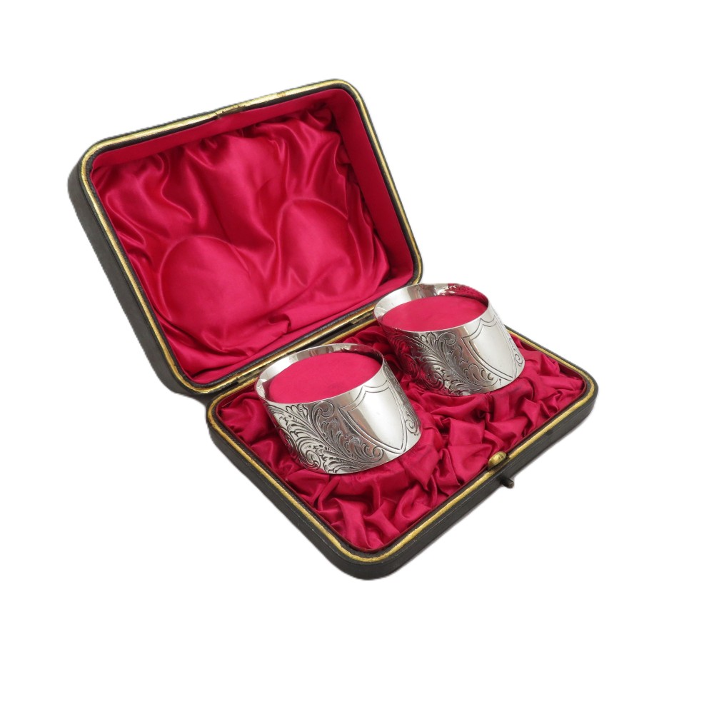 A pair of engraved Victorian sterling silver napkin rings set inside a red silk and velvet lined presentation box.