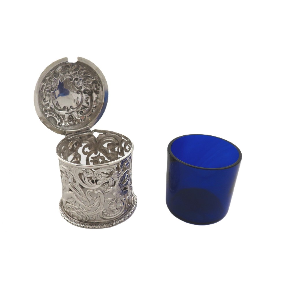 A Victorian sterling silver mustard pot featuring pierced scrollwork and cherub design with a cobalt blue glass liner and matching spoon. View III