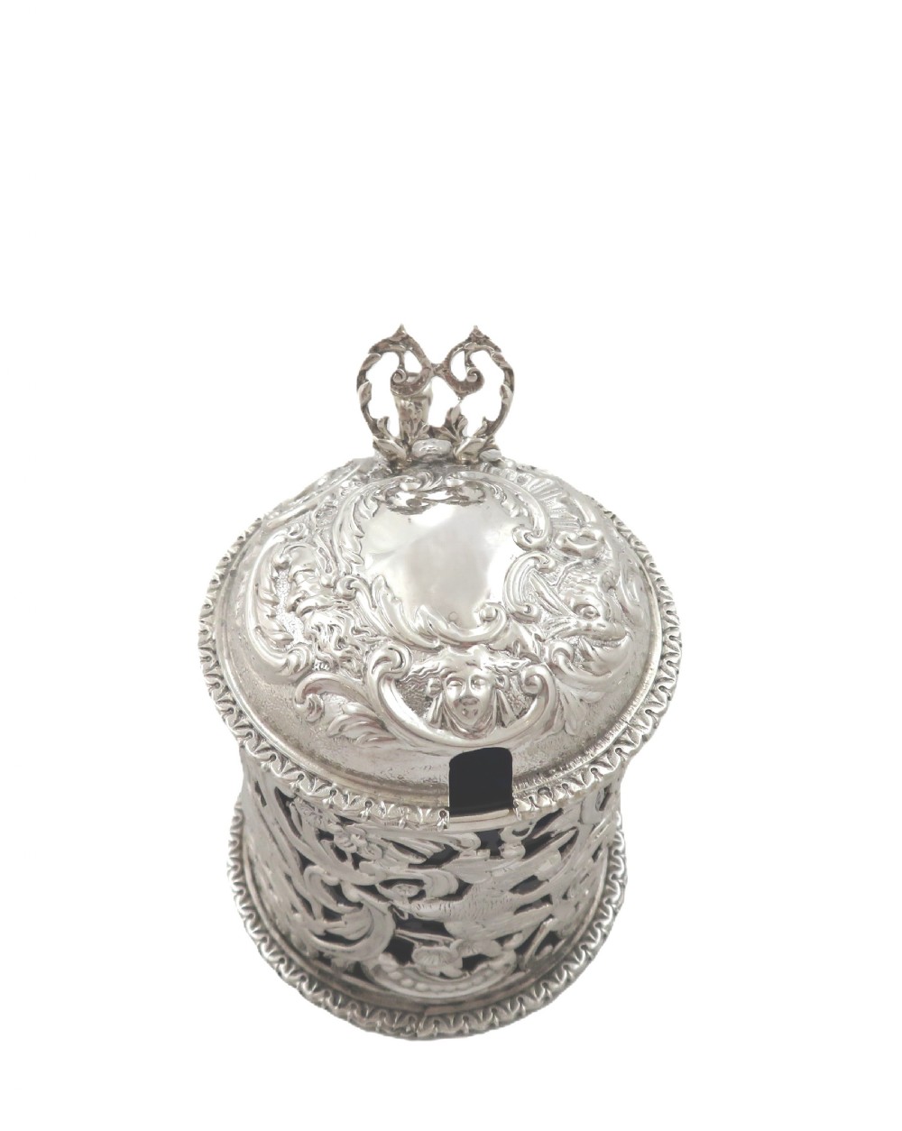 A Victorian sterling silver mustard pot featuring pierced scrollwork and cherub design with a cobalt blue glass liner and matching spoon. View VII