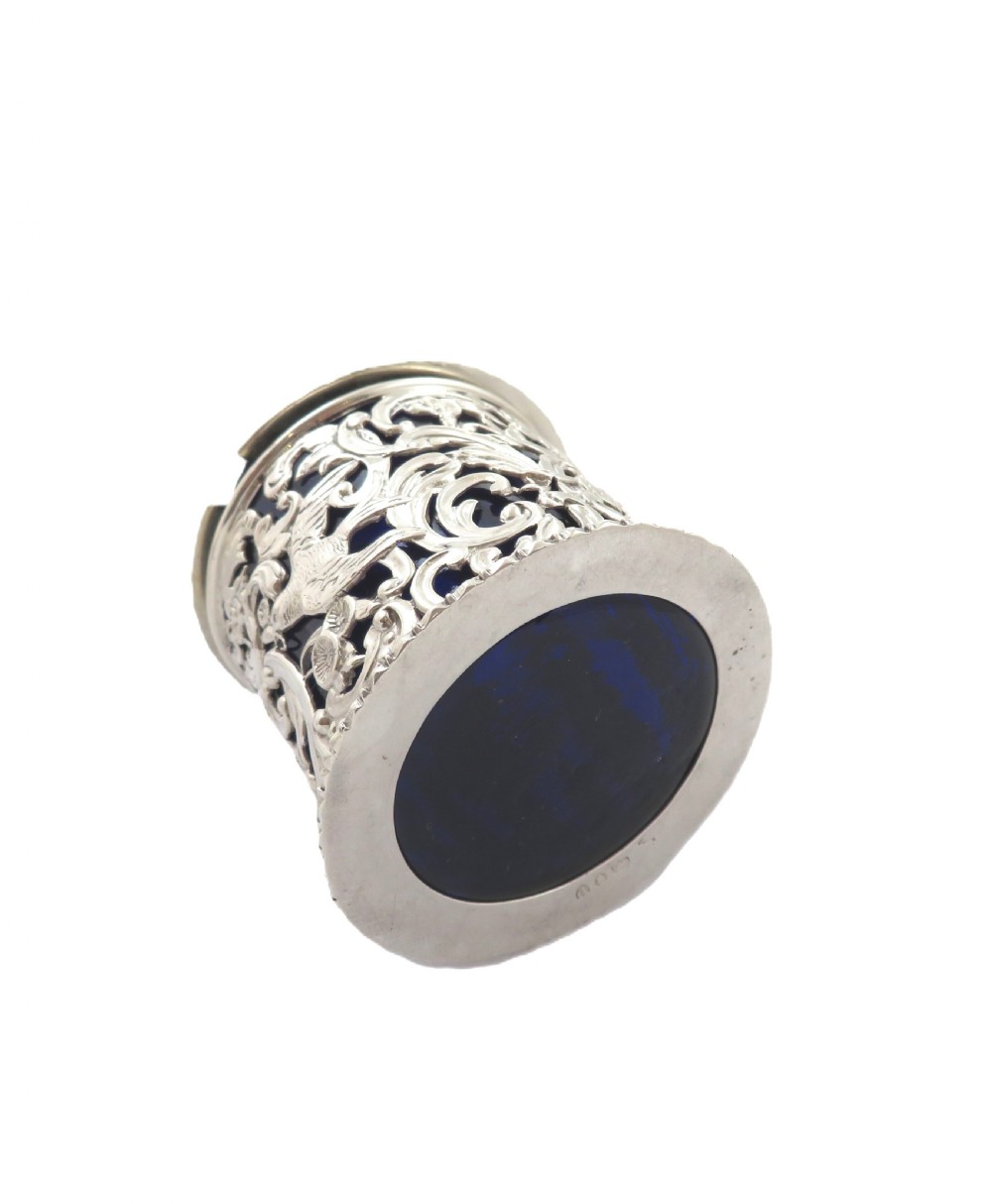 A Victorian sterling silver mustard pot featuring pierced scrollwork and cherub design with a cobalt blue glass liner and matching spoon. View X