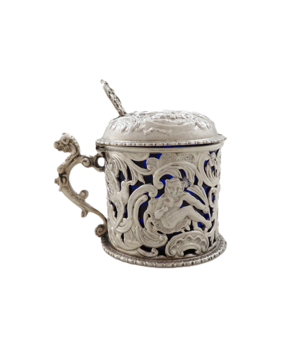 A Victorian sterling silver mustard pot featuring pierced scrollwork and cherub design with a cobalt blue glass liner and matching spoon. View XI