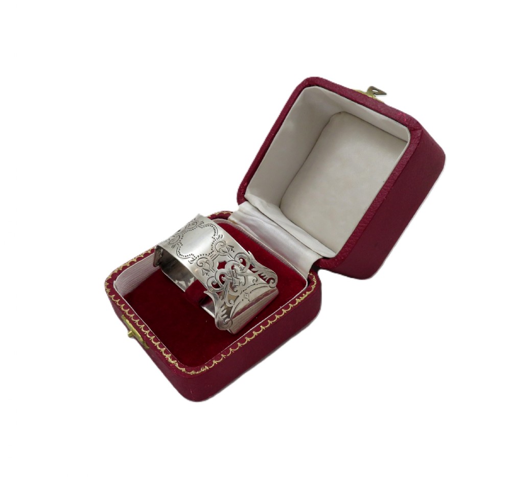 An engraved sterling silver napkin ring resting inside an open red leather presentation case lined with dark red velvet and cream silk. View X