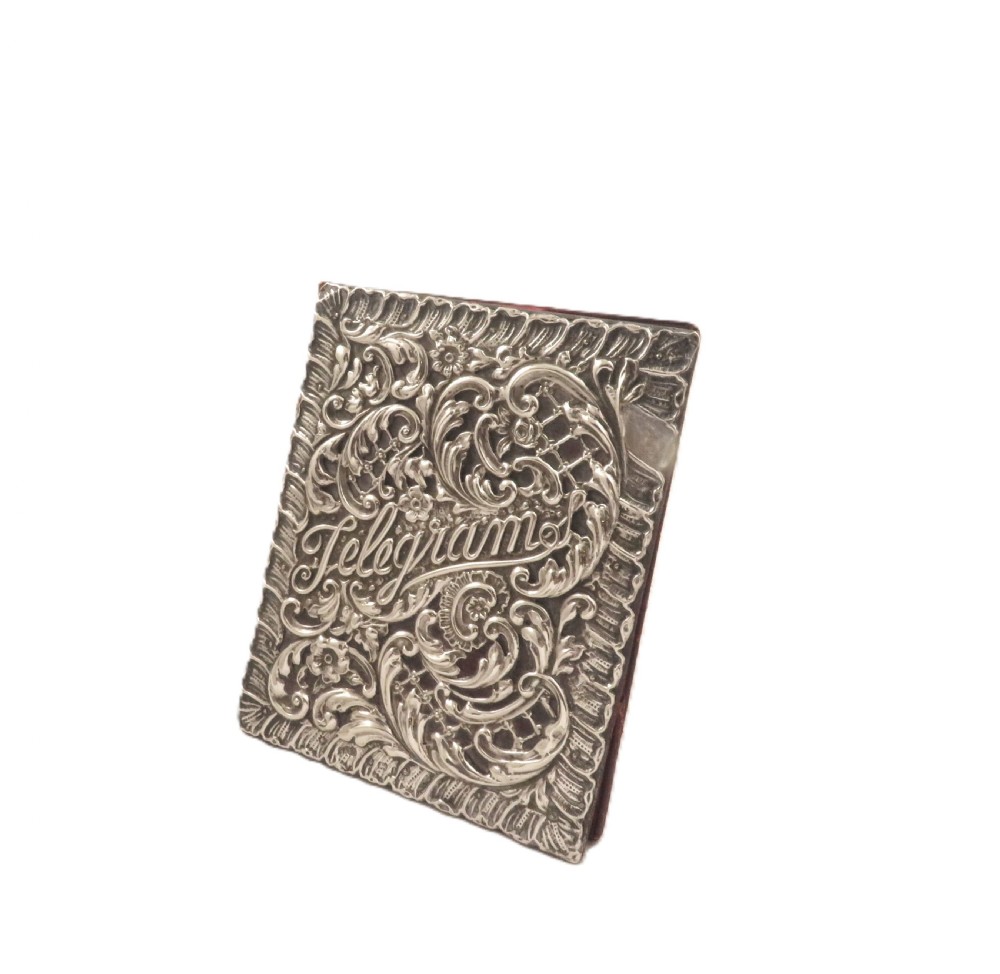 An Edwardian sterling silver telegram folder cover featuring relief scrollwork, floral motifs, and embossed lettering reading Telegrams. View IV