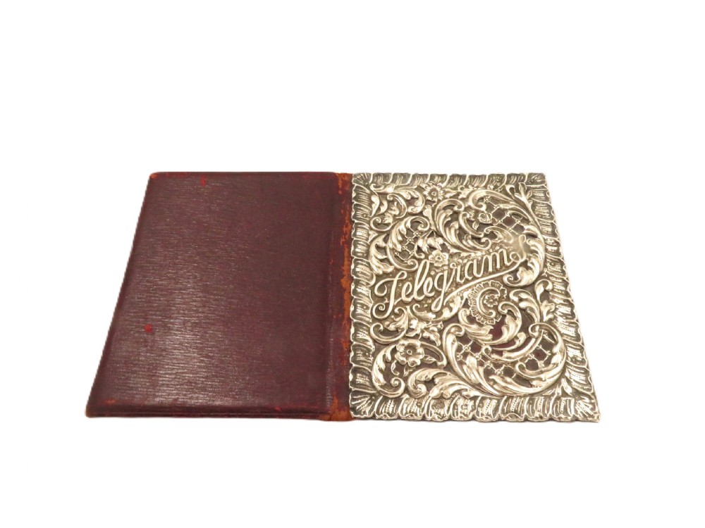 An Edwardian sterling silver telegram folder cover featuring relief scrollwork, floral motifs, and embossed lettering reading Telegrams. View V