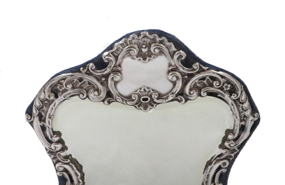 A Victorian sterling silver easel mirror featuring intricate floral repousse decoration and a dark blue velvet backing. View III