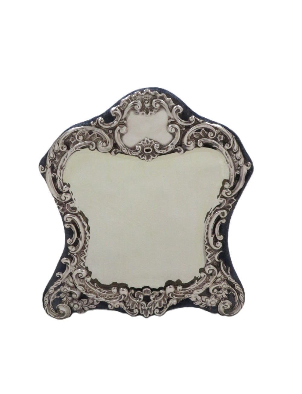 A Victorian sterling silver easel mirror featuring intricate floral repousse decoration and a dark blue velvet backing. View V