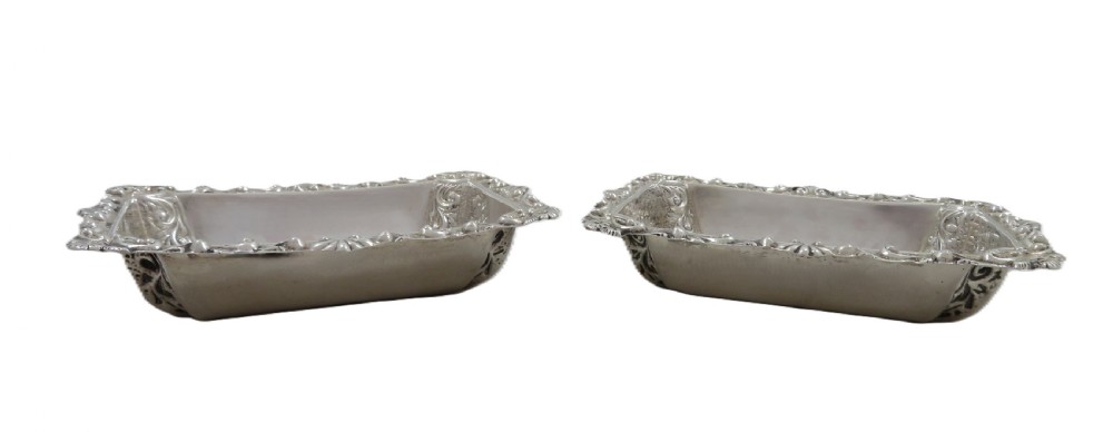 A pair of rectangular embossed sterling silver dishes with ornate scrolled borders, displayed inside a silk and velvet-lined dark presentation case. View IV