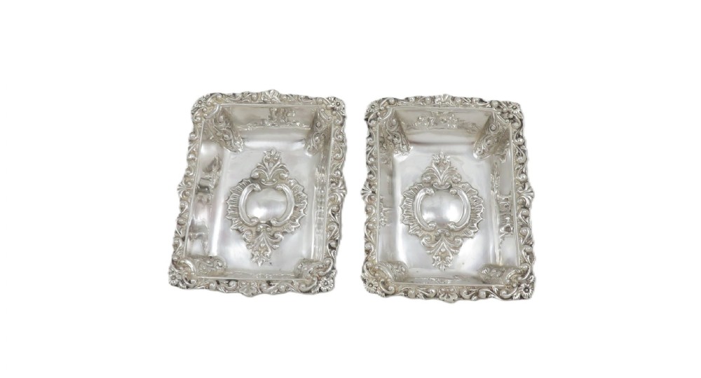 A pair of rectangular embossed sterling silver dishes with ornate scrolled borders, displayed inside a silk and velvet-lined dark presentation case. View VIII