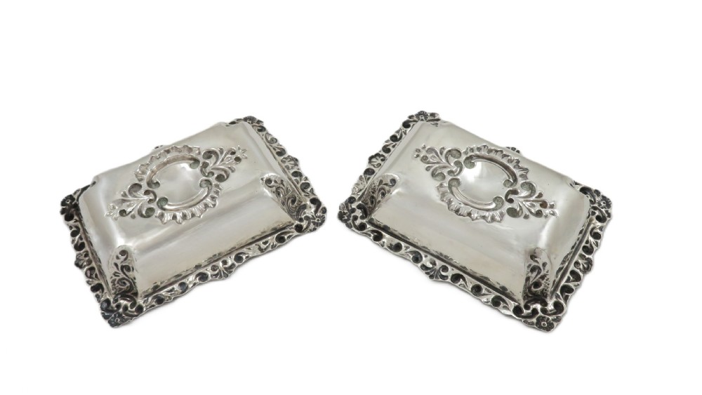 A pair of rectangular embossed sterling silver dishes with ornate scrolled borders, displayed inside a silk and velvet-lined dark presentation case. View IX