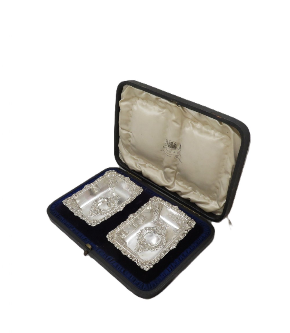 A pair of rectangular embossed sterling silver dishes with ornate scrolled borders, displayed inside a silk and velvet-lined dark presentation case. View XI