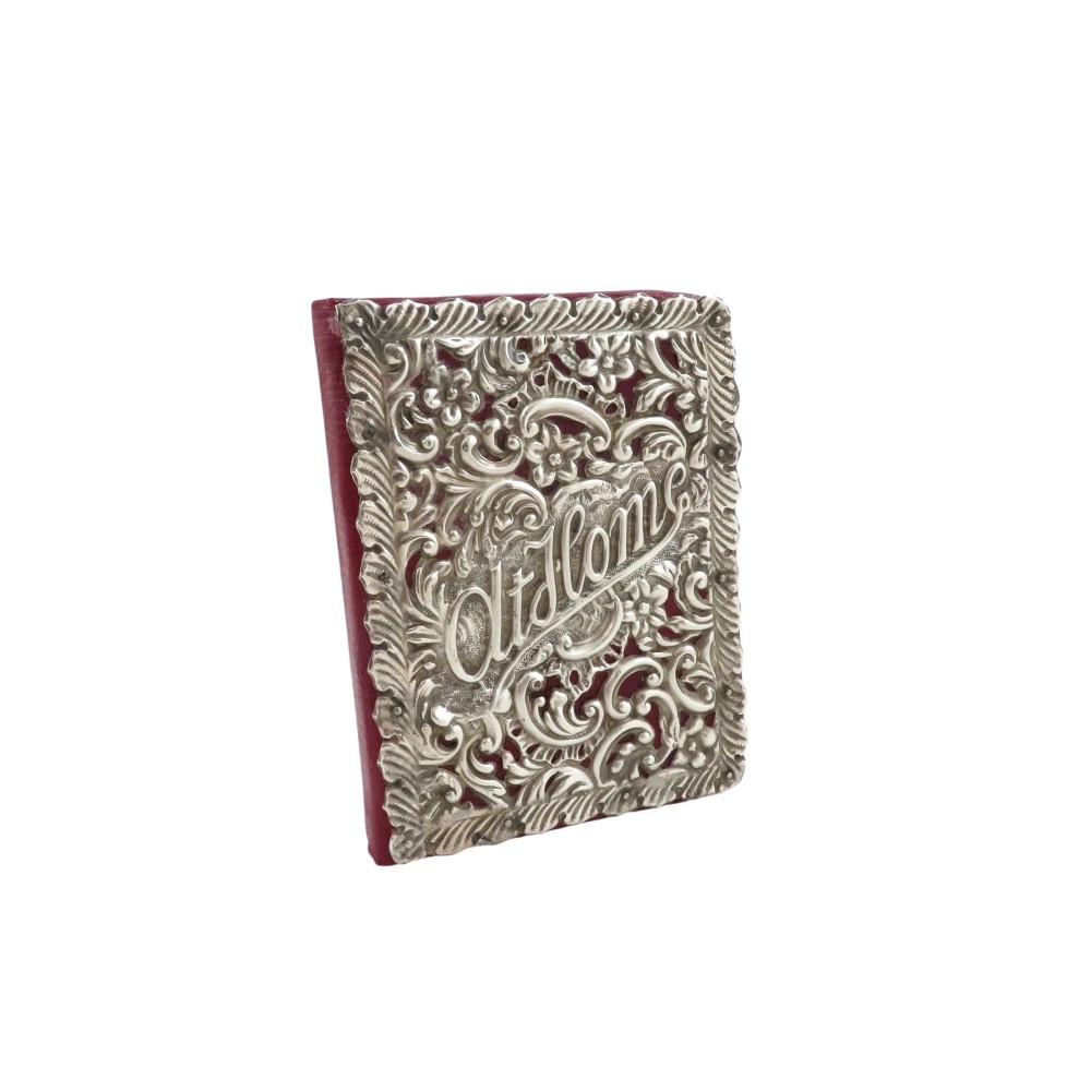 An Edwardian sterling silver fronted At Home book featuring intricate pierced floral scrollwork over a crimson leather binding.