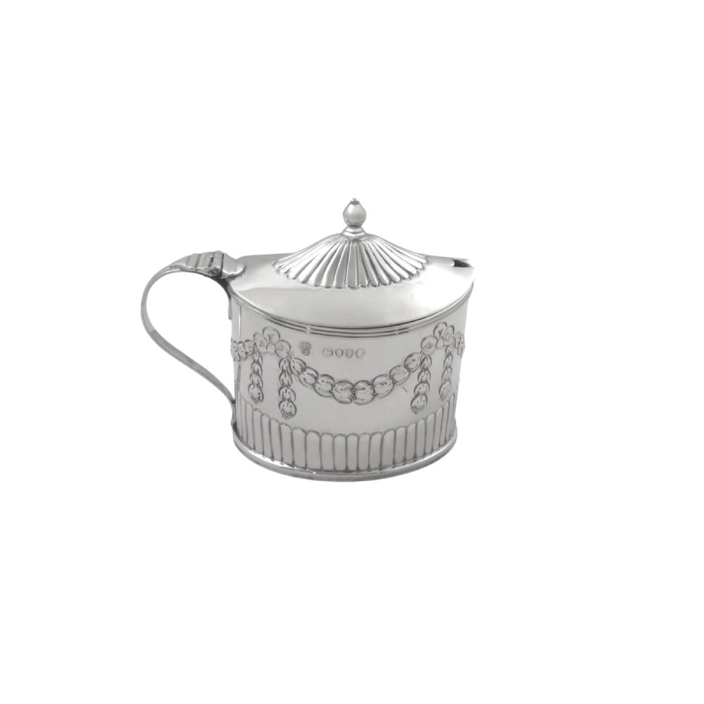 Victorian sterling silver mustard pot featuring embossed festoon swags, a fluted lid with finial, and visible British hallmarks.