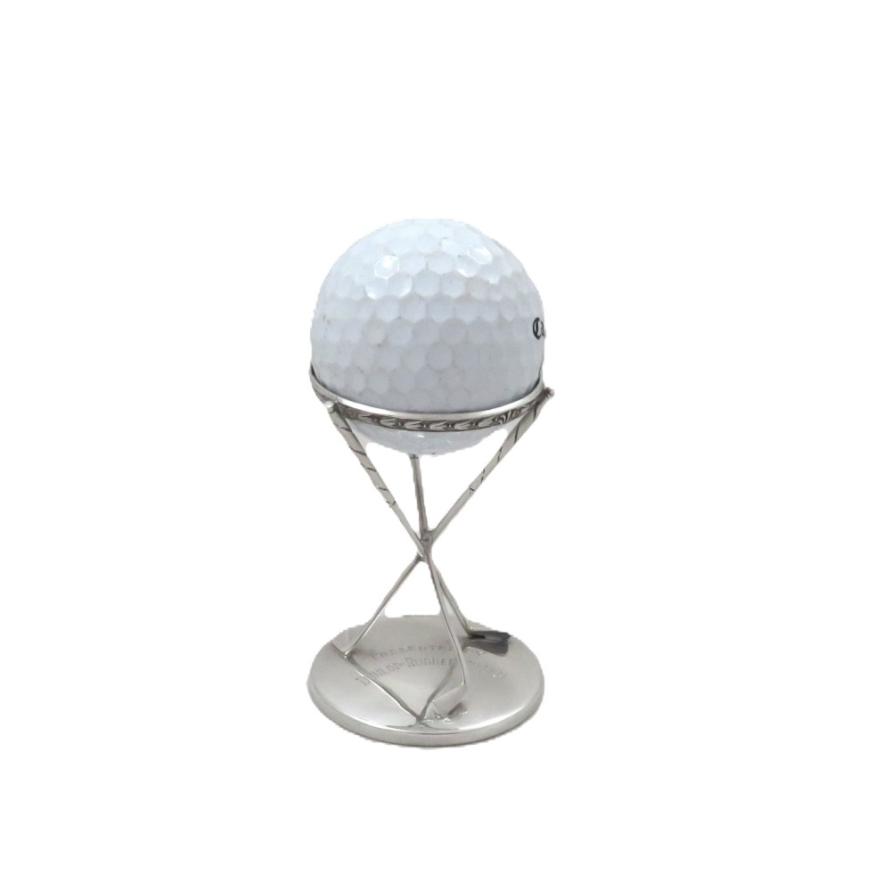 A sterling silver golf ball stand featuring three crossed golf club legs supported by a circular silver base holding a white golf ball.