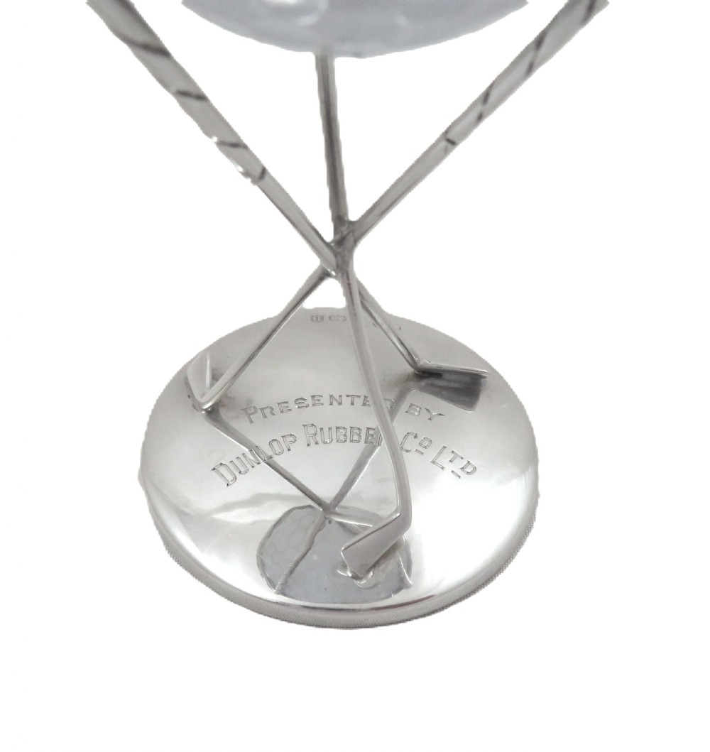 A sterling silver golf ball stand featuring three crossed golf club legs supported by a circular silver base holding a white golf ball. View IV