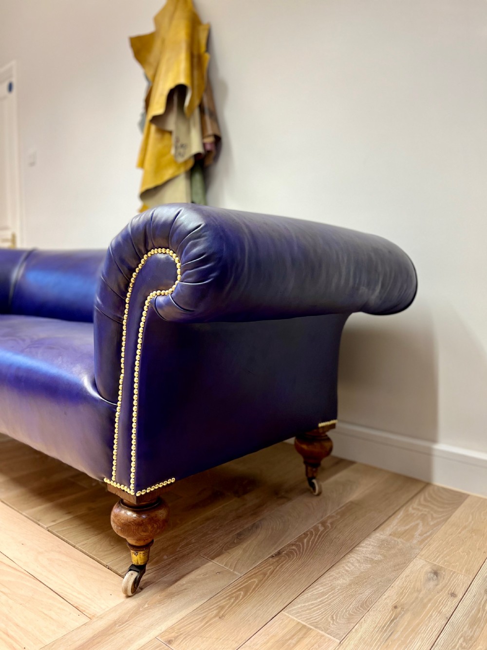 A Victorian Chesterfield sofa featuring hand-dyed purple leather upholstery, brass studding, and turned timber legs with castors. View VI