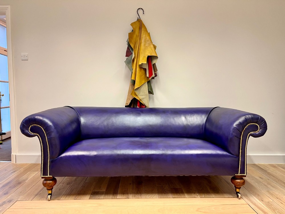 A Victorian Chesterfield sofa featuring hand-dyed purple leather upholstery, brass studding, and turned timber legs with castors. View VII