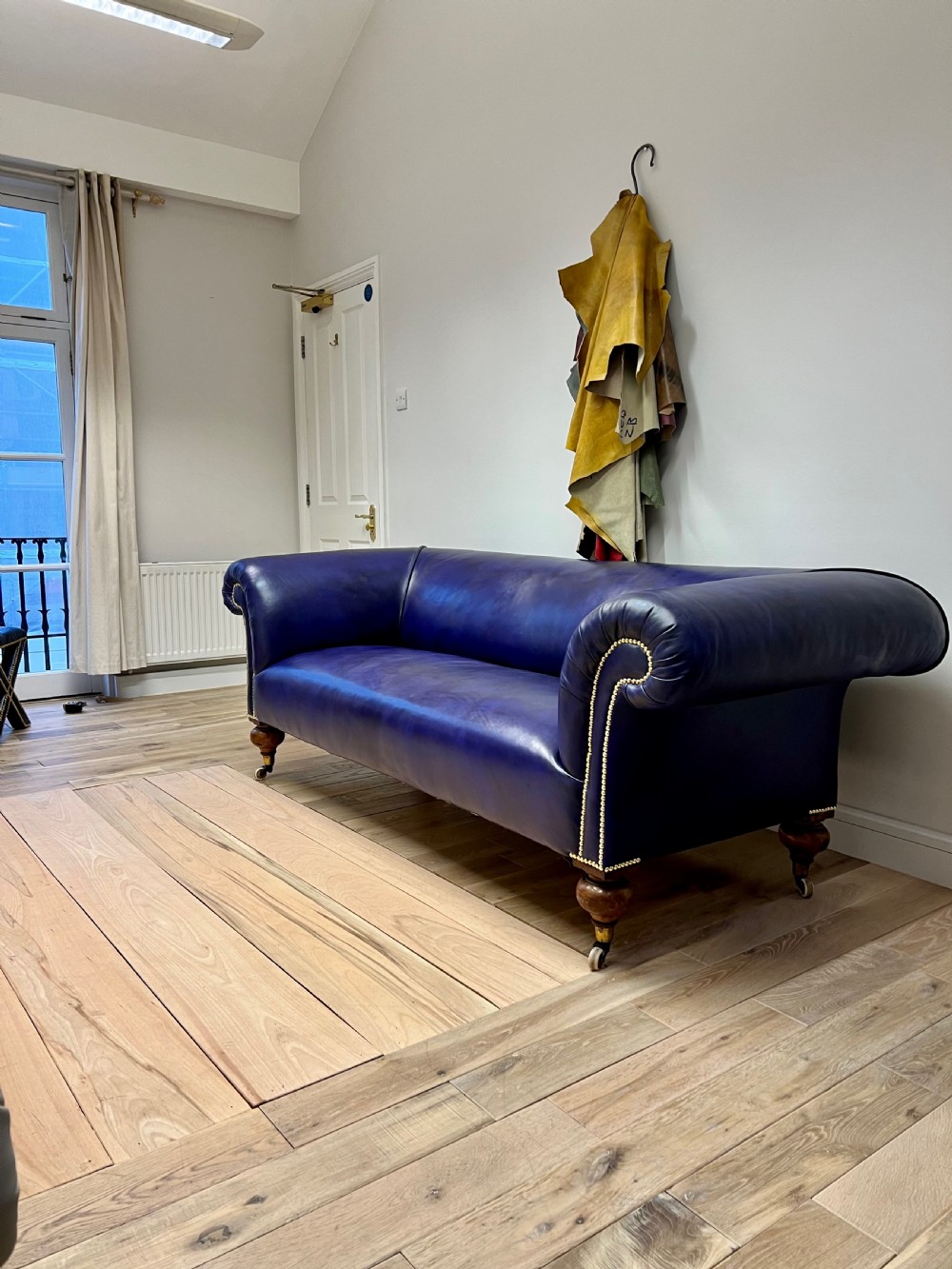 A Victorian Chesterfield sofa featuring hand-dyed purple leather upholstery, brass studding, and turned timber legs with castors. View IX