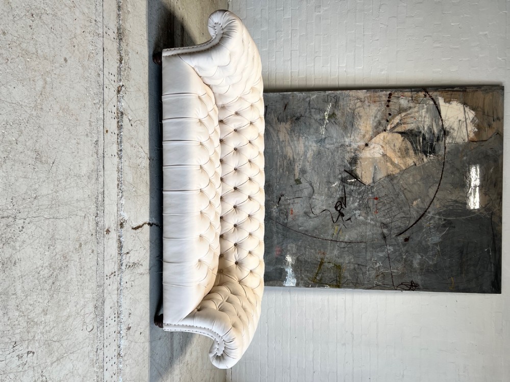 A restored 19th-century Victorian Chesterfield sofa upholstered in natural off-white undyed leather with deep buttoning and turned wood legs. View V