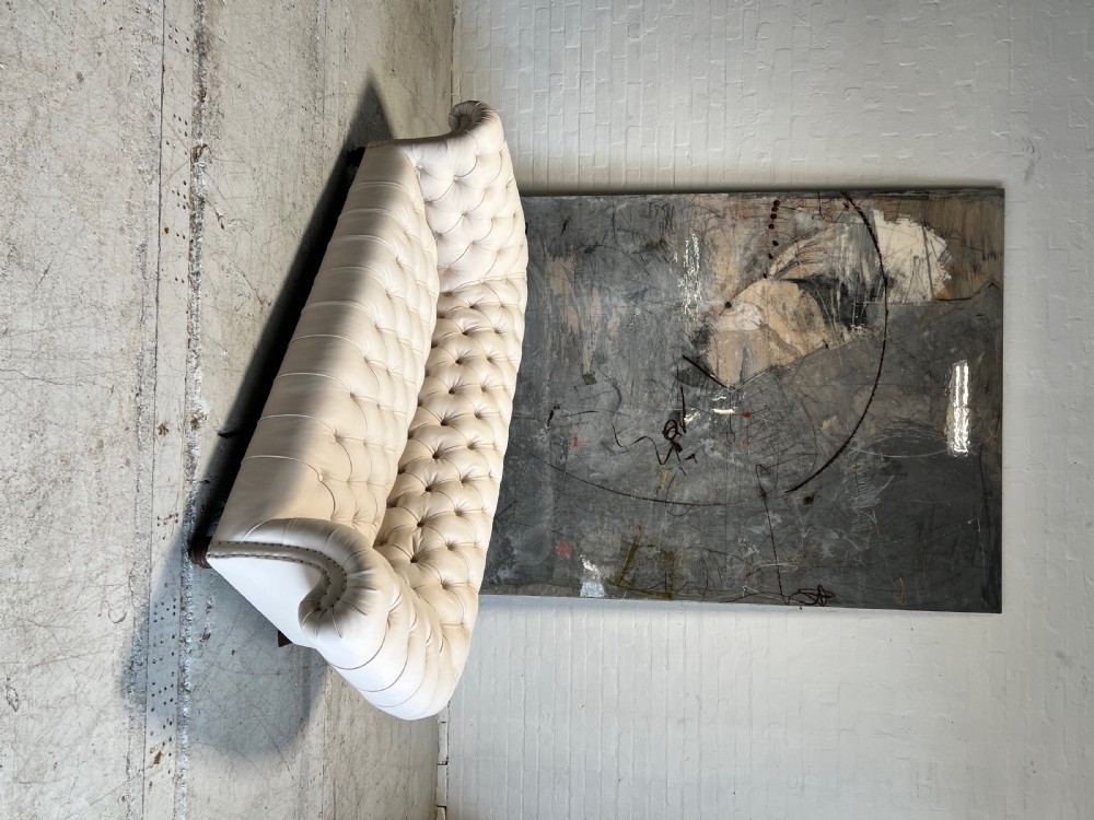 A restored 19th-century Victorian Chesterfield sofa upholstered in natural off-white undyed leather with deep buttoning and turned wood legs. View VI