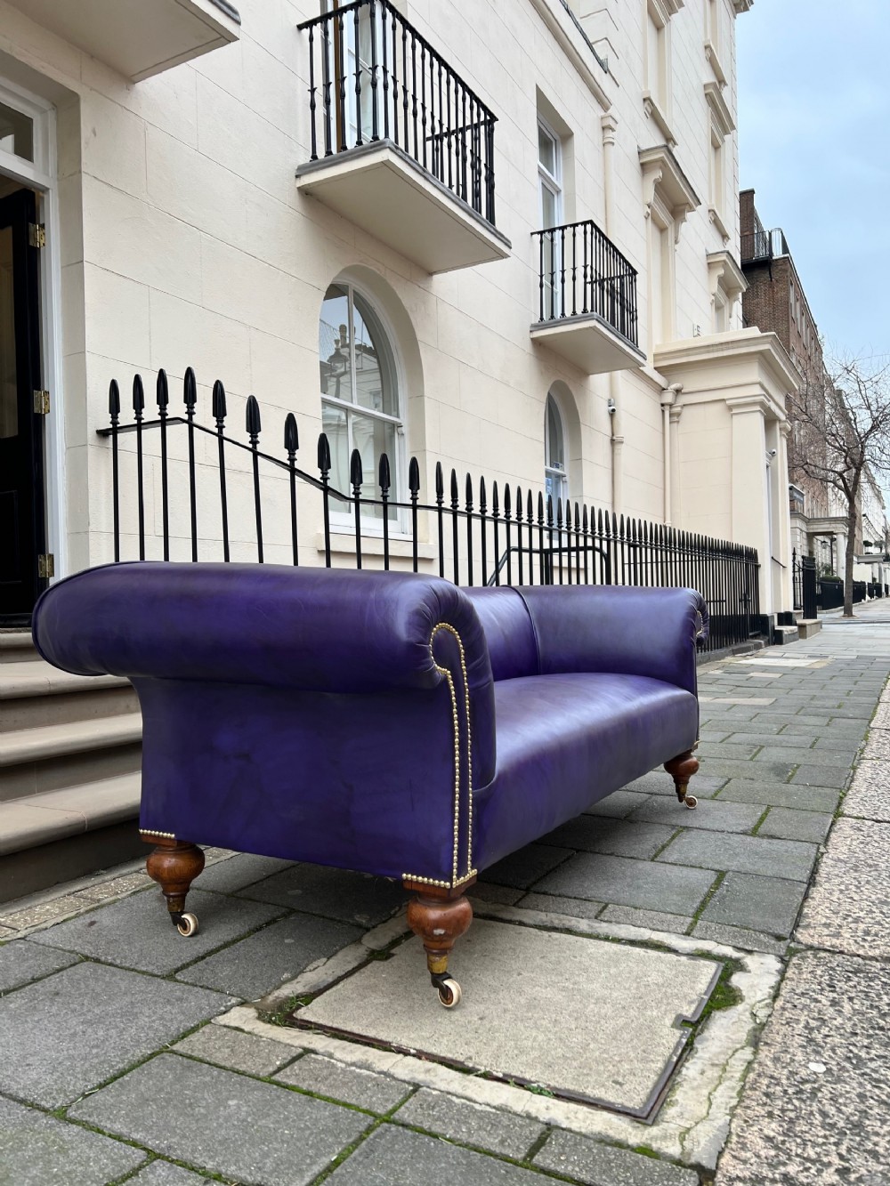 A Victorian Chesterfield sofa featuring hand-dyed purple leather upholstery, brass studding, and turned timber legs with castors.
