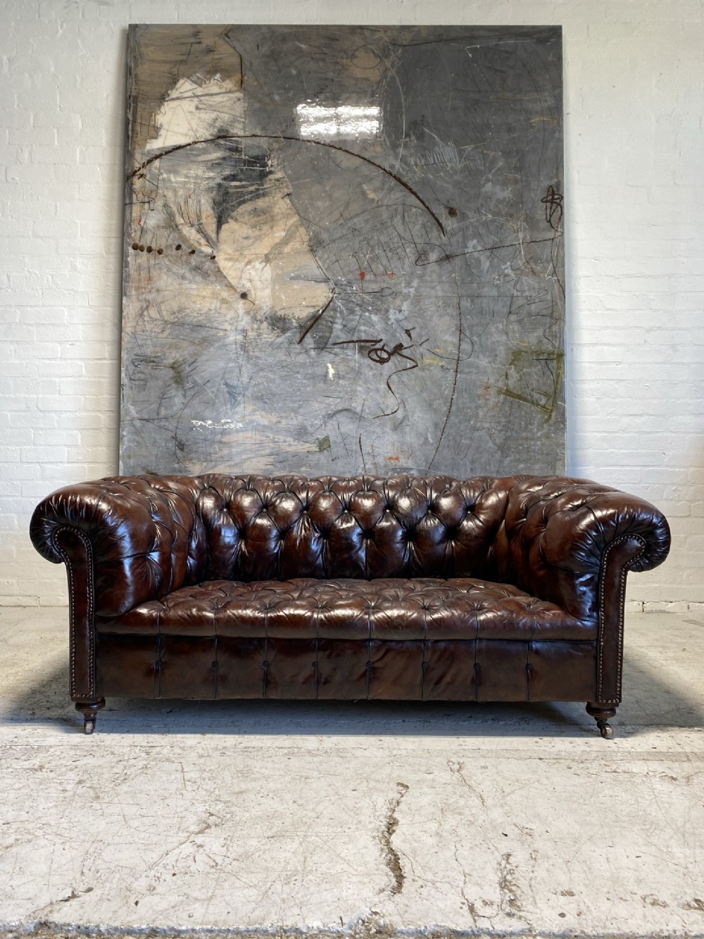 A nineteenth-century dark brown leather Chesterfield sofa featuring deep buttoned tufting, rolled arms, and brass studding detail.