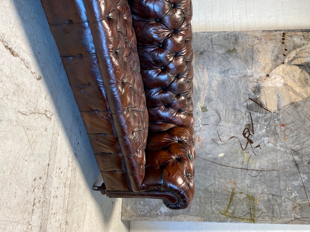 A nineteenth-century dark brown leather Chesterfield sofa featuring deep buttoned tufting, rolled arms, and brass studding detail. View II