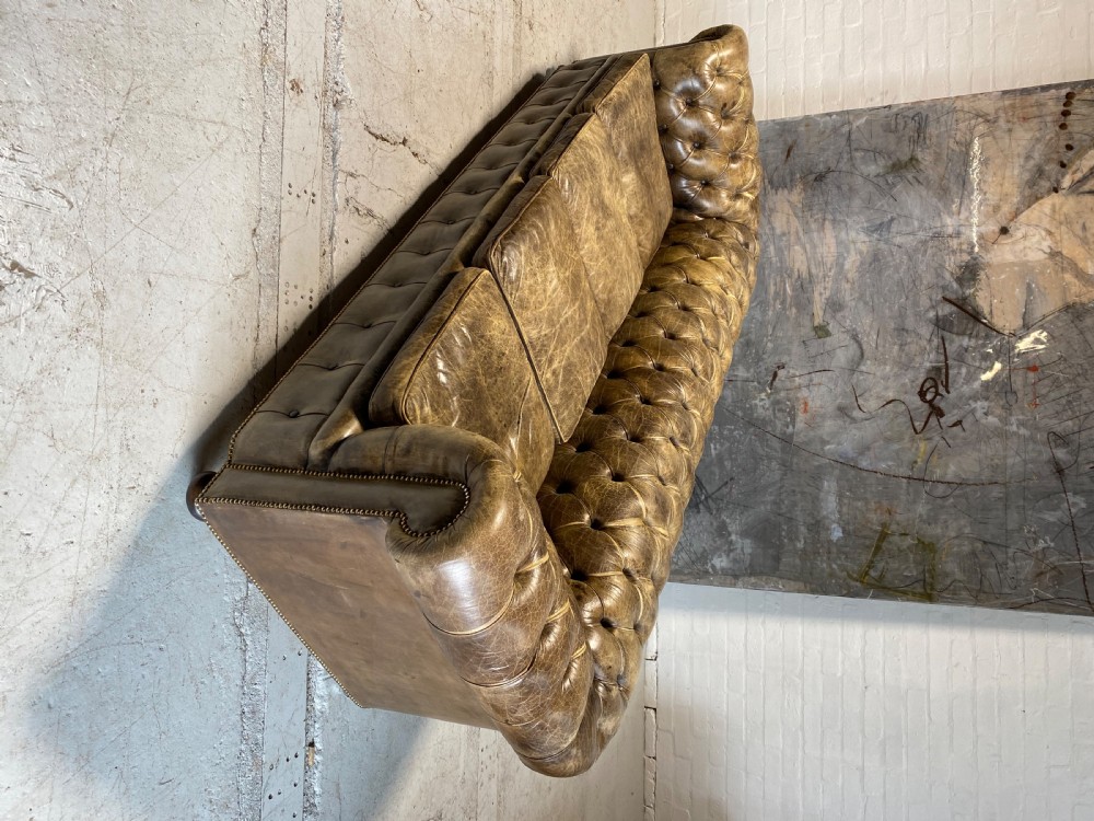 A large mid-century four-cushion Chesterfield sofa upholstered in distressed tan leather with deep button tufting, rolled arms, and brass stud trim. View VIII