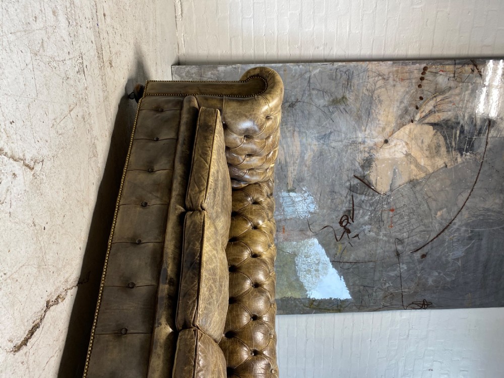 A large mid-century four-cushion Chesterfield sofa upholstered in distressed tan leather with deep button tufting, rolled arms, and brass stud trim. View IX