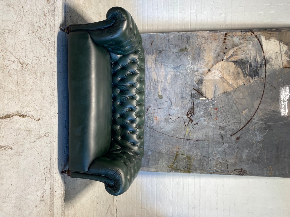 A 19th-century Chesterfield sofa upholstered in British Racing Green leather, featuring deep button tufting, rolled arms, studded trim, and turned timber feet on castors. View IV
