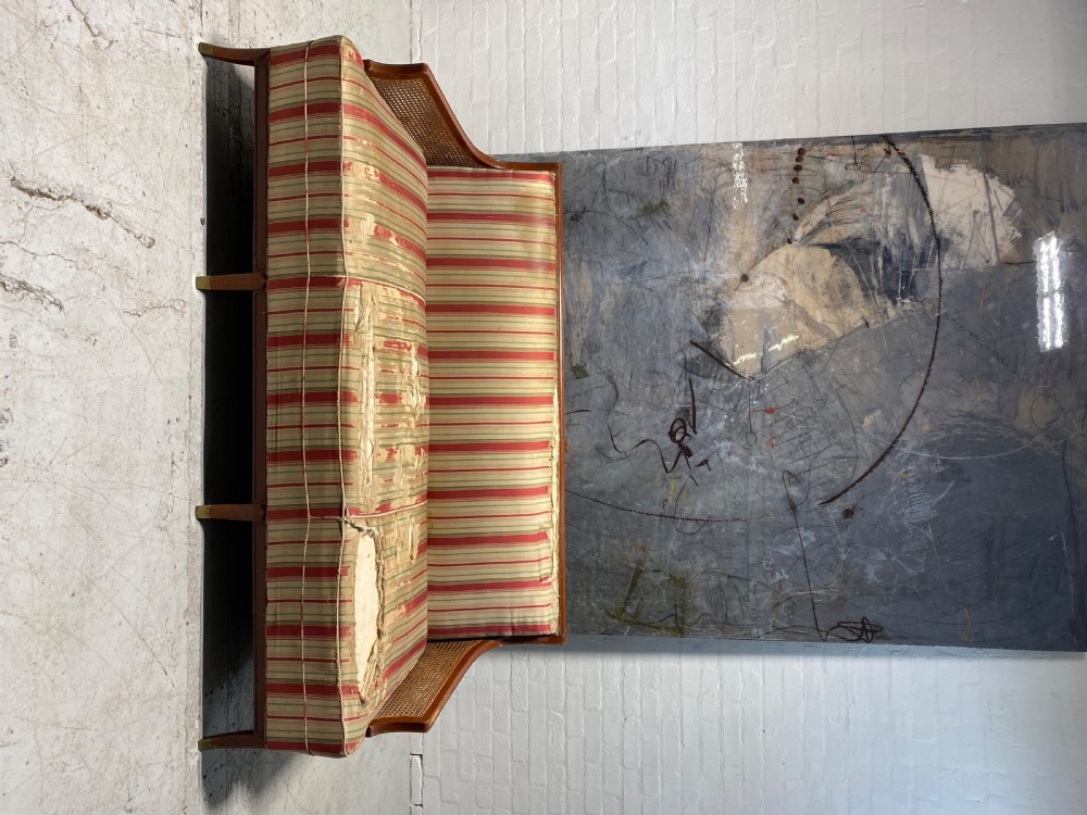 An Art Deco caned sofa featuring a mahogany frame, woven cane side panels, tapered legs with brass feet, and worn striped upholstery. View IV