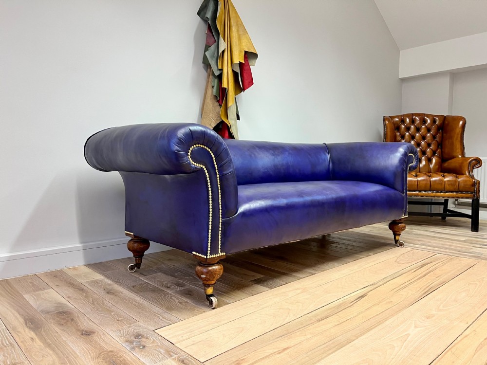 A 19th-century rolled arm sofa upholstered in hand-dyed amethyst purple leather with brass stud decoration and turned wooden legs on brass castors. View II