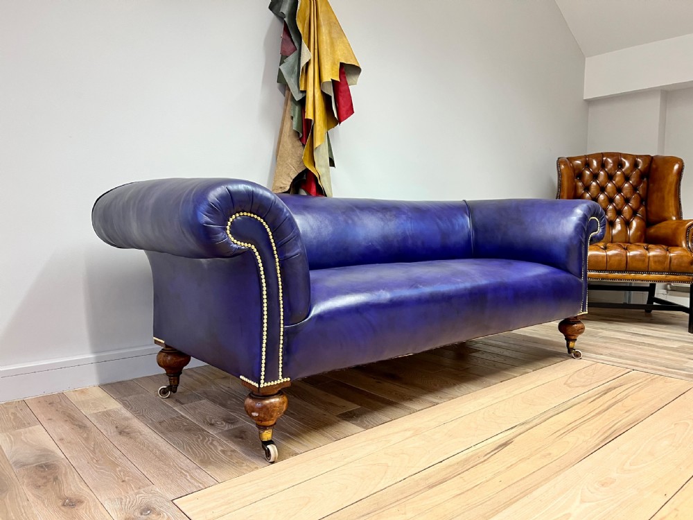 A 19th-century rolled arm sofa upholstered in hand-dyed amethyst purple leather with brass stud decoration and turned wooden legs on brass castors. View IV