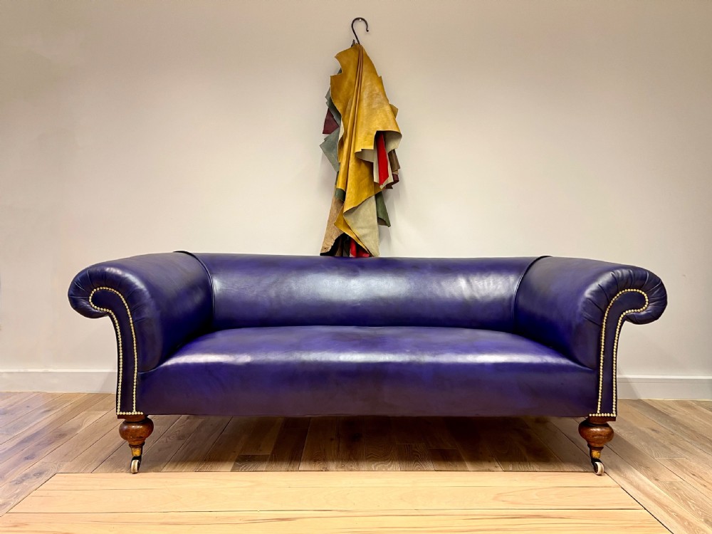 A 19th-century rolled arm sofa upholstered in hand-dyed amethyst purple leather with brass stud decoration and turned wooden legs on brass castors. View V