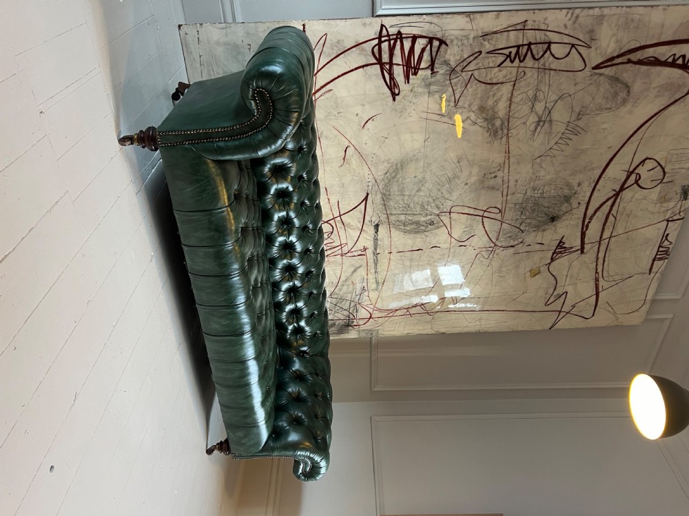 A nineteenth-century green leather Chesterfield sofa featuring deep button tufting, rolled arms with brass nailhead trim, and turned mahogany legs on brass castors. View III