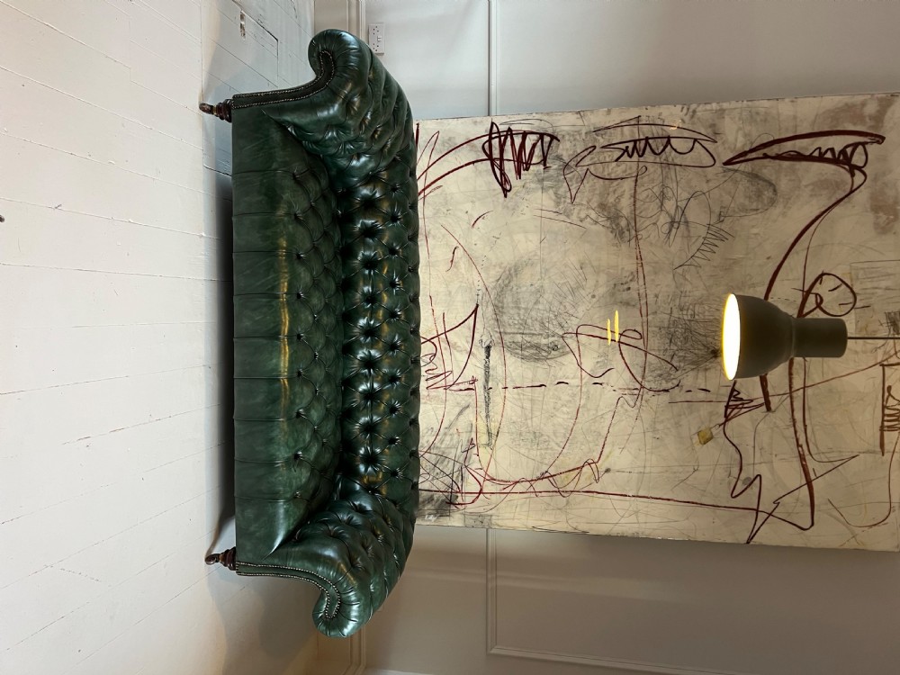 A nineteenth-century green leather Chesterfield sofa featuring deep button tufting, rolled arms with brass nailhead trim, and turned mahogany legs on brass castors. View V
